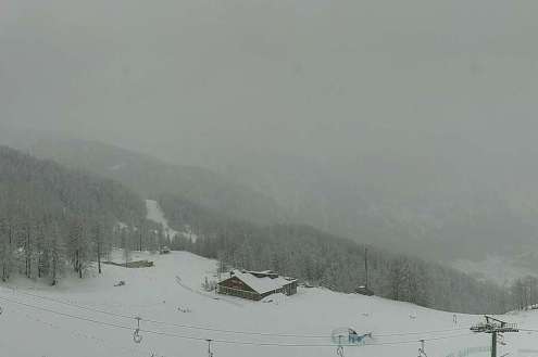 Snow falling over the snow-covered slopes of Bardonecchia, Italy, with mountain building in the background surrounded by snow-covered trees – Weather to ski – Today in the Alps, 27 February 2024